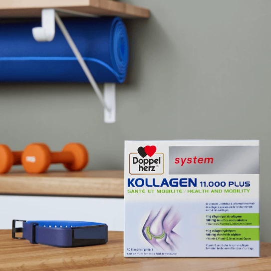 A box of Doppelherz Kollagen 11,000 Plus is displayed on a wooden surface, promoting health and mobility. It features a colorful label with the product name and benefits. Nearby, there are orange dumbbells, a blue exercise mat, and a fitness tracker, suggesting a focus on wellness and fitness.